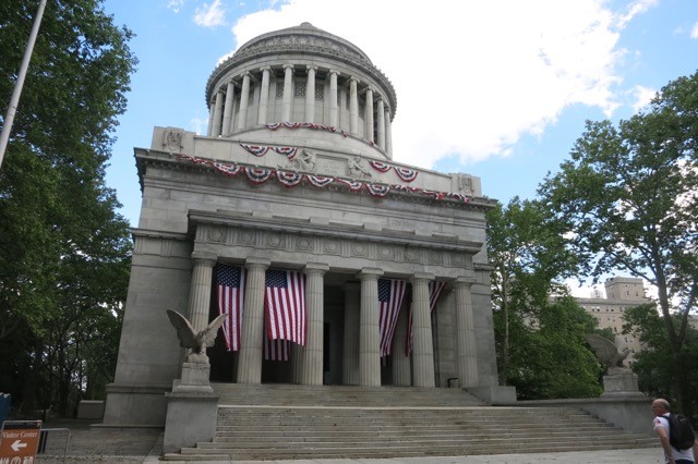 a stone building with columns and flags with General Grant National Memorial in the background