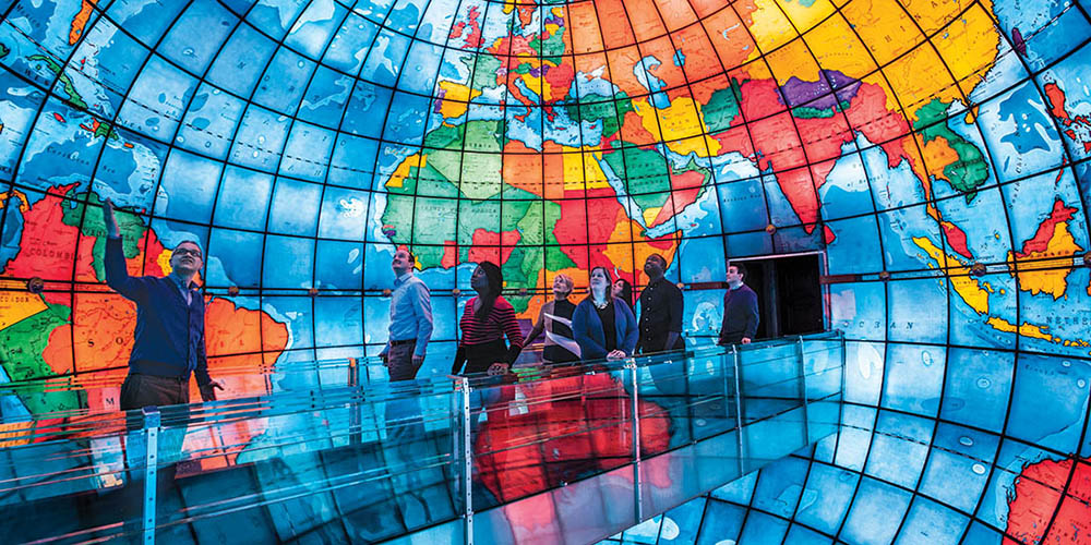 a group of people standing on a glass walkway with Mapparium in the background