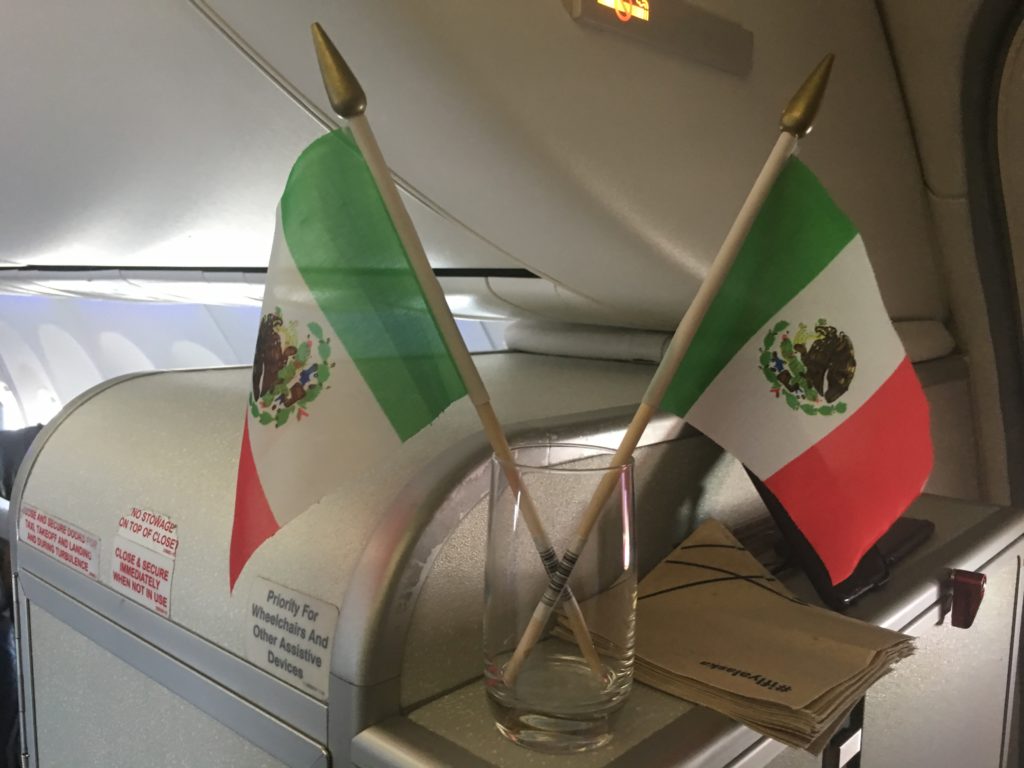 Two small Mexico flags resting in an Alaska Airlines drink glass on the closet in front of the first class cabin