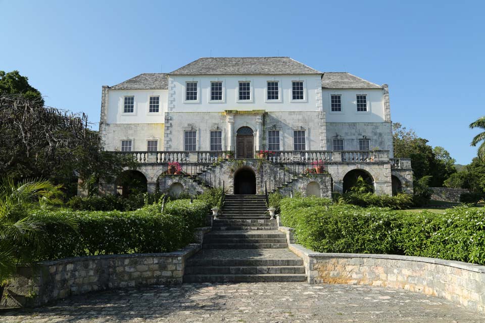 a large white building with a stone staircase leading to the front with White Witch of Rose Hall in the background