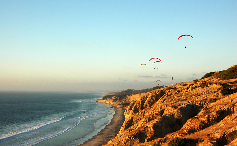 a group of paragliders flying over a cliff by the ocean