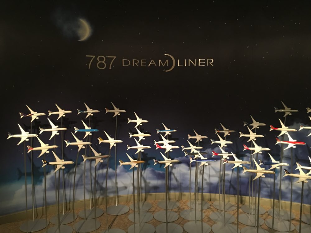 An assortment of Boeing 787 model airplanes held up on posts in front of a dark blue wall with clouds painted on the bottom. The 787 Dreamliner logo appears on the upper part of the wall, underneath a painted moon.