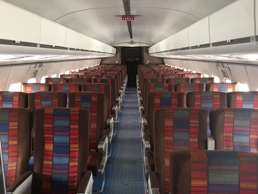 The interior of an airplane with a red, orange, and blue 1970s-era color scheme on the seats
