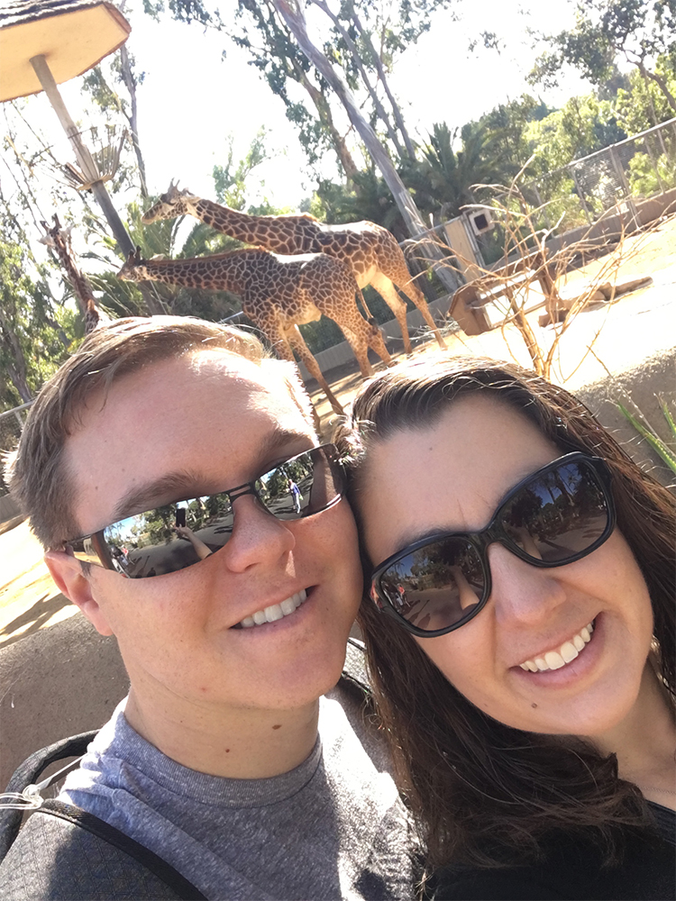 a man and woman taking a selfie with giraffes in the background