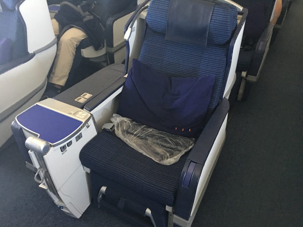A photo of a business class seat with a pillow and blanket on top.